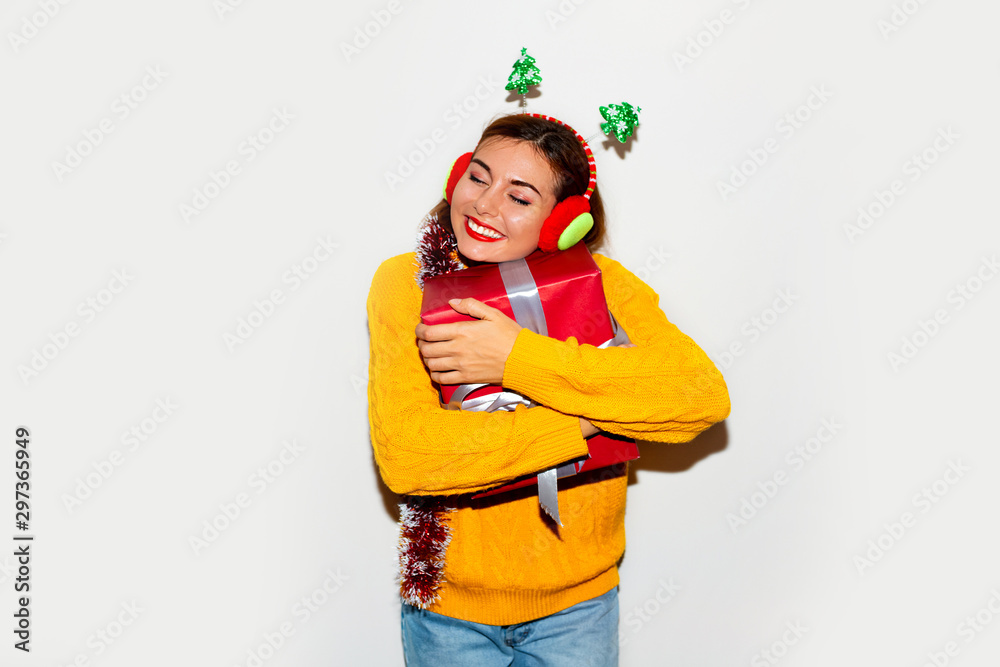 Lovable european girl with christmas present expressing happiness. Refined cute young woman in yellow knitted sweater laughing on grey background in new year. Lovable european girl with christmas present expressing happiness. Refined cute young woman in yellow knitted sweater laughing on grey background in new year.