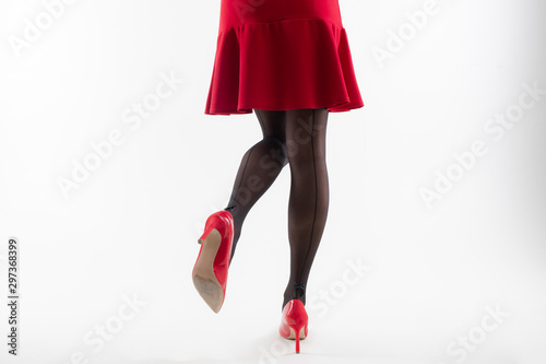Close up of a girl's legs in painted pantyhose on heels and in a red dress on a white background