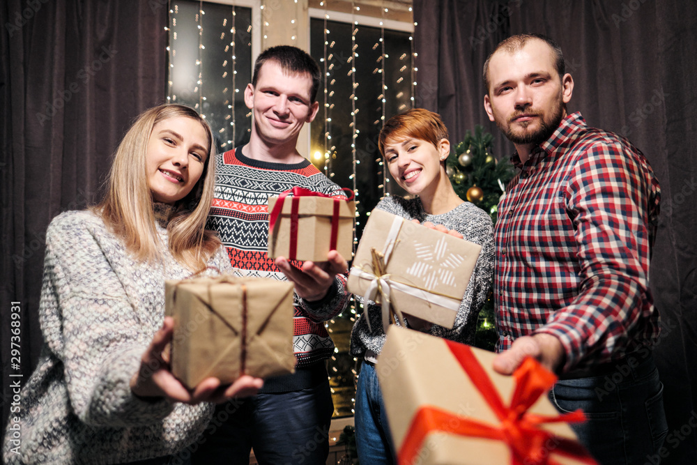 Obraz premium A group of friends, men and women, celebrate Christmas. They give each other presents, rejoice and laugh. New Years Eve.