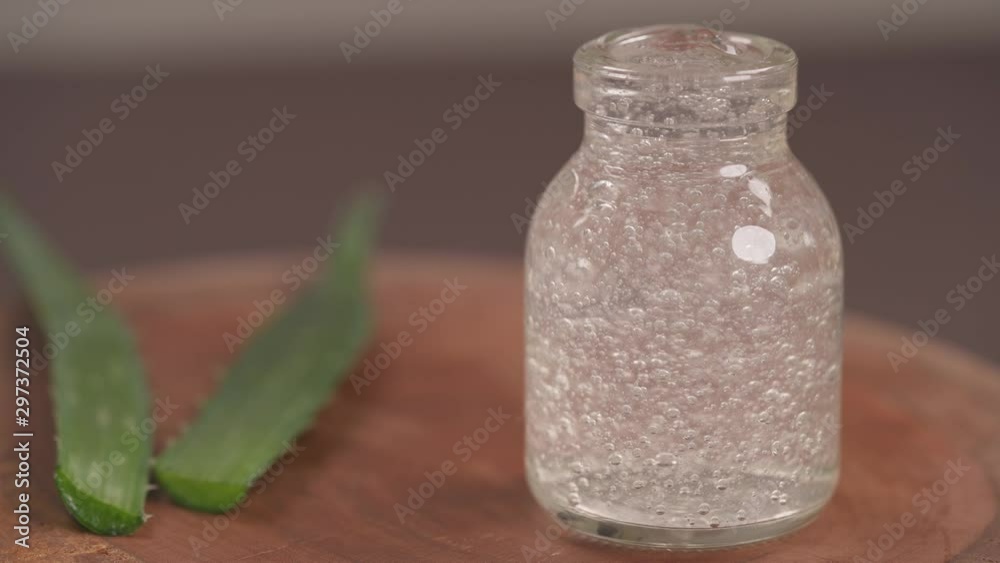 Top bottom shot of a glass bottle filled with aloe vera gel. Leaves of aloe vera plant on blurred background. Natural organic renewal cosmetics for sensitive skin. Selective focus