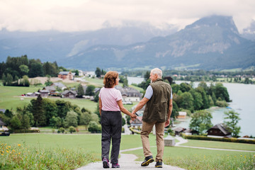 Rear view of senior pensioner couple hiking in nature, holding hands.