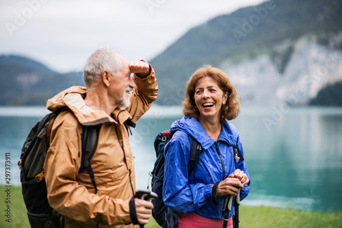 A senior pensioner couple hiking by lake in nature, talking.