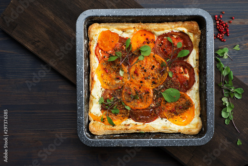 Tarte (pie) with soft cream cheese, colorful tomatoes and spices in a square baking dish on a wooden board.