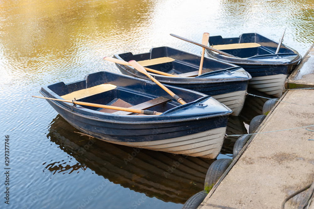 Close up of three blue and white rowing boats moored on a tranquil river on a sunny day Close up of three blue and white rowing boats moored on a tranquil river on a sunny day