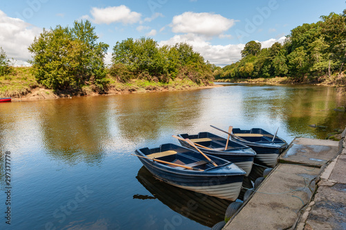 Three blue and white rowing boats moored on a tranquil river on a sunny day