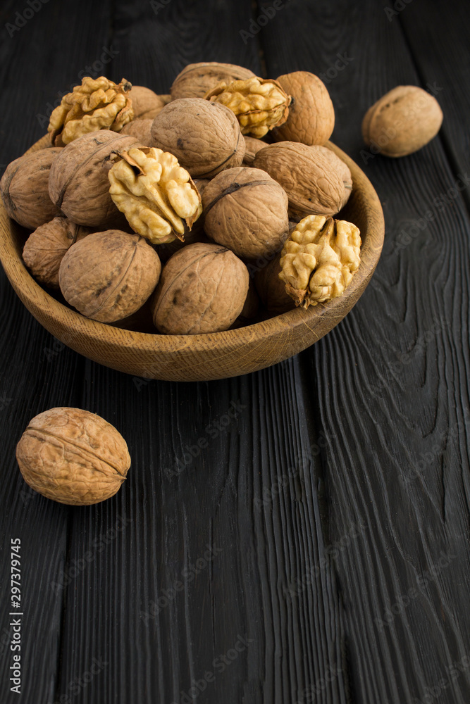 Walnuts in the brown bowl on the black wooden background. Copy space. Location vertical. Walnuts in the brown bowl on the black wooden background. Copy space. Location vertical.