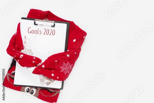 Creative winter flat lay.Knitted gray sweater with a notebook for writing 2020 on a white background with copy space, concept for new year plans and motivation and goal setting