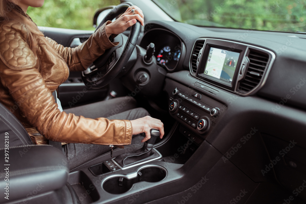 woman in summer autumn, driving car, parking reversing, engages automatic transmission. Start movement of car, inclusion of parking mode. Leather jacket, touch screen.interior of car.