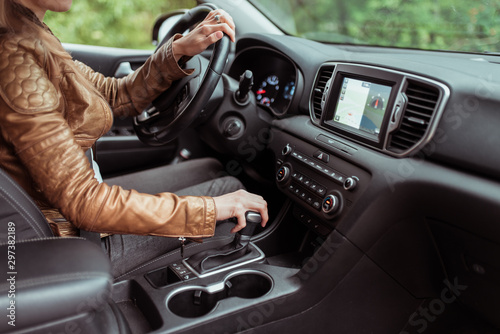 woman in summer autumn, driving car, parking reversing, engages automatic transmission. Start movement of car, inclusion of parking mode. Leather jacket, touch screen.interior of car. photo