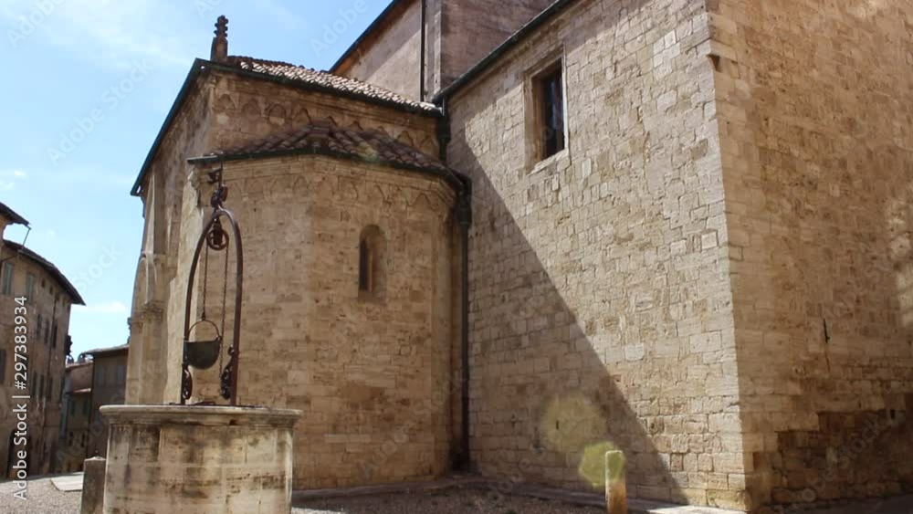 Tilt-Up HD Video of a water well with a soldier's helmet and in the background the collegiate Church of San Quirico D'Orcia, Siena, Tuscany, Italy. Video HD