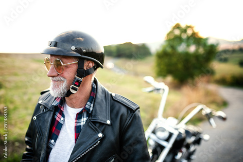 A cheerful senior man traveller with motorbike in countryside, walking.