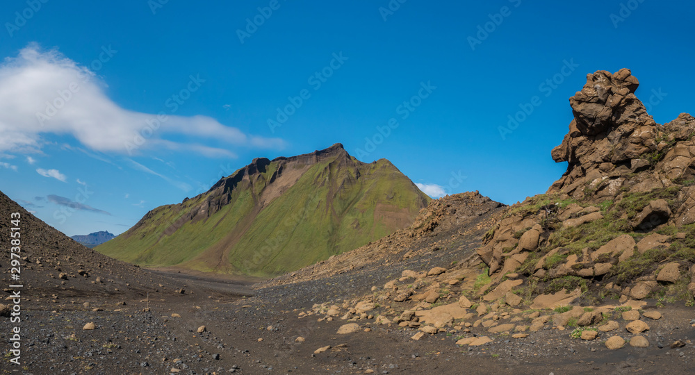 Panoramic volcanic desert landscape with lava rock formation and green Hattafell mountain with footpath of Laugavegur trail. Fjallabak Nature Reserve, Iceland. Summer blue sky