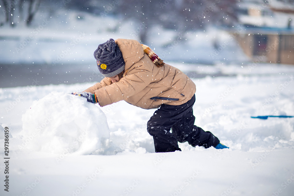 Boy having fun, playing outside, surrounded with snow, making snowball.
