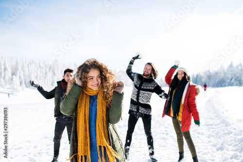 A group of young friends on a walk outdoors in snow in winter forest.