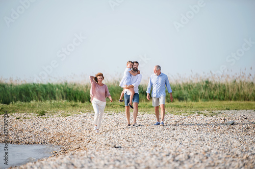 Multigeneration family on a holiday walking by the lake, holding hands. © Halfpoint