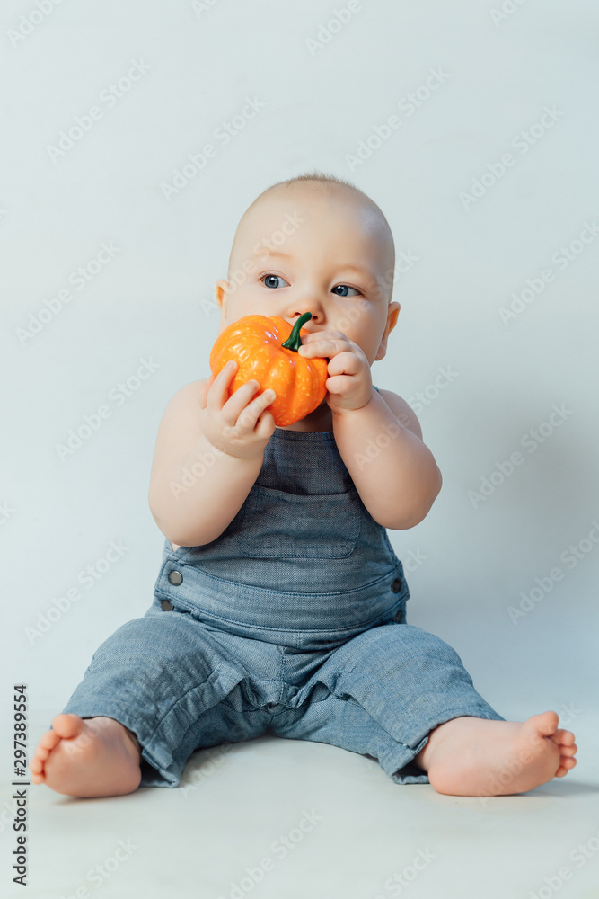 Little baby sitting on the floor and playing with a small orange pumpkin. Halloween concept Little baby sitting on the floor and playing with a small orange pumpkin. Halloween concept