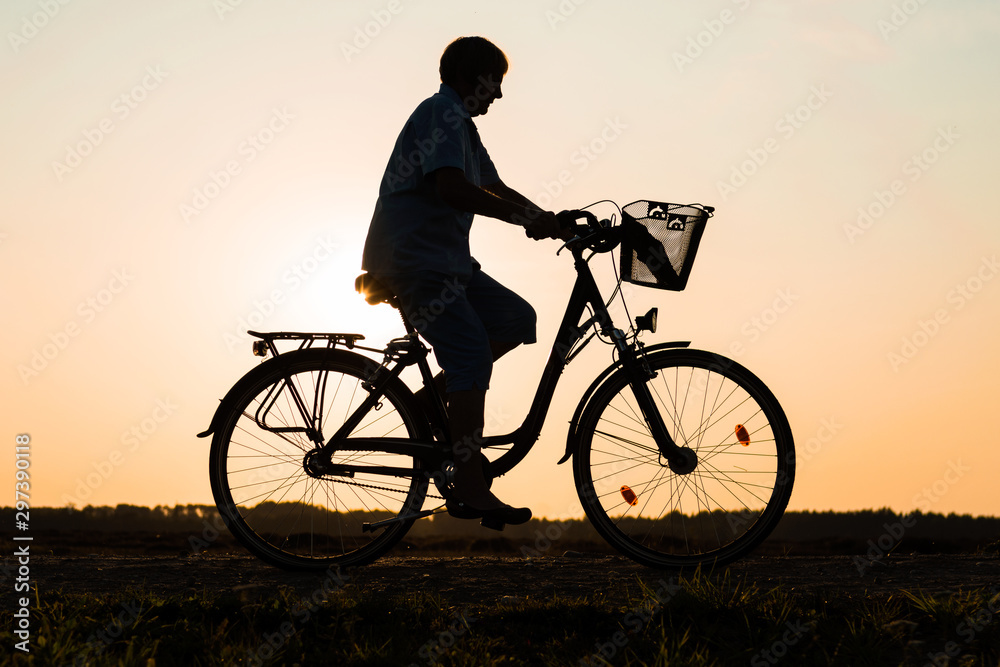 Senior woman riding bike in nature, silhouette of riding woman at sunset Senior woman riding bike in nature, silhouette of riding woman at sunset