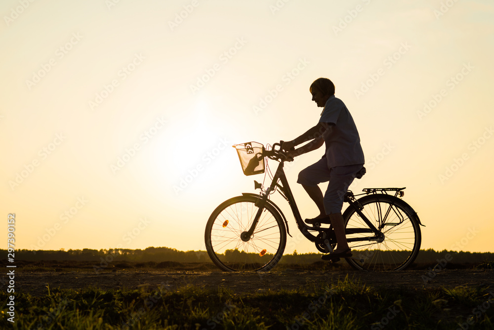 Senior woman riding bike in nature, silhouette of riding woman at sunset Senior woman riding bike in nature, silhouette of riding woman at sunset