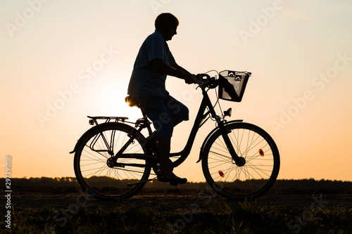 Senior woman riding bike in nature, silhouette of riding woman at sunset