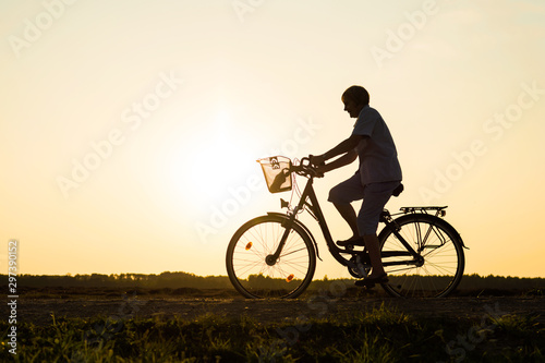 Senior woman riding bike in nature, silhouette of riding woman at sunset