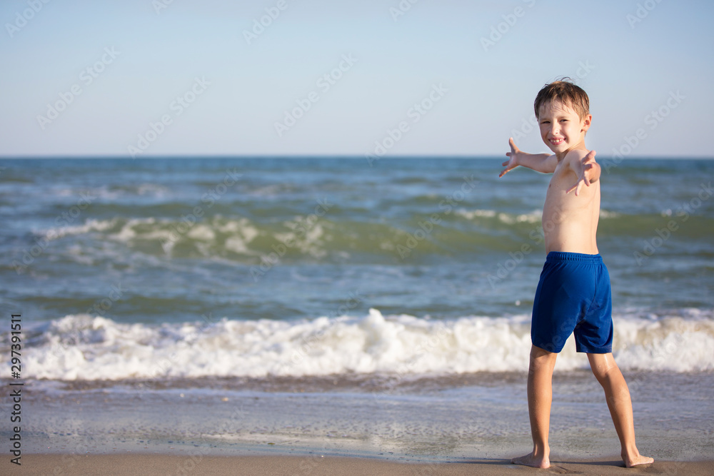 Joyful boy near the sea opened his arms. Child resting on the beach