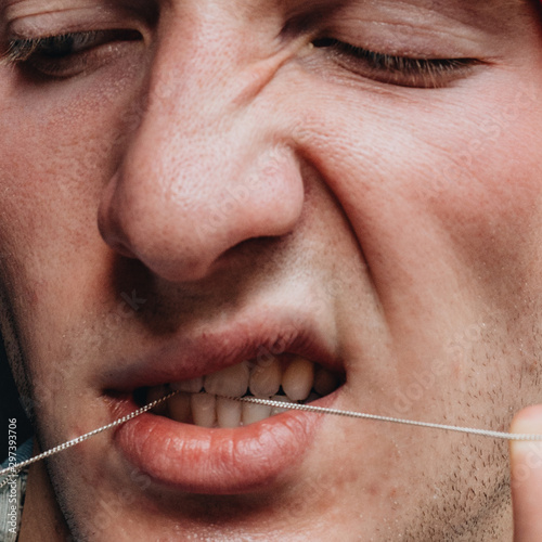 Close up view of young man pulling string between his teeth photo