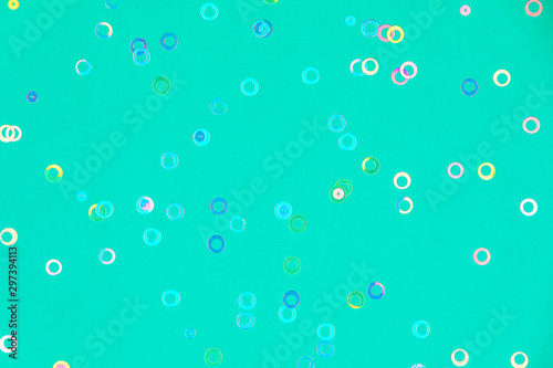 Colorful holographic foil confetti background. Pastel colored pink, blue and yellow circles and stars sparse on trendy mint green colored paper. Simple holiday concept. Top view, flat lay