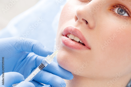Cosmetology Service. Young woman at beauty clinic lying while doctor in gloves doing injection of hyaluronic acid into lips close-up