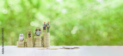 Saving for retirement and pension fund concept : Senior retired couple, vintage clock, US dollar money bag, deposit saving jar on steps of rising coins, depicts long-term investment for aging society