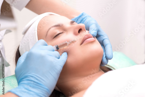 injection into the skin of the face of a young woman, close-up. A cosmetologist with a syringe with a needle introduces a means to remove wrinkles on the face in the lip area.