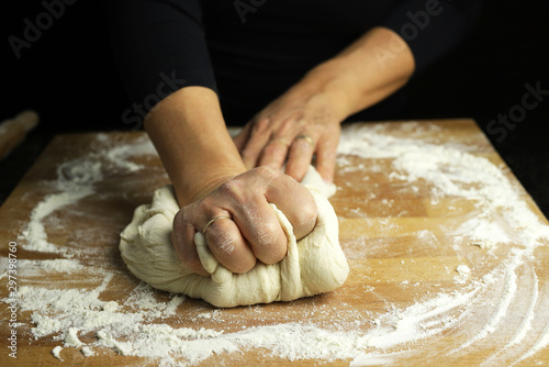 Preparare la tradizionale pasta fatta in casa. Primo piano delle mani della donna che impastano pasta fresca per produrre pane o pizza su una tavola infarinata