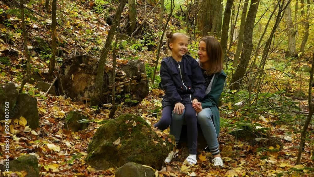Autumn forest. Woman and teenager girl sitting on the log and carelessly talking. Autumn forest. Woman and teenager girl sitting on the log and carelessly talking.