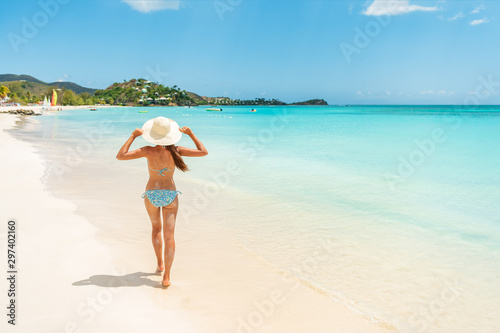 Foto Beach travel vacation woman walking on luxury Caribbean cruise destination Antigua island in bikini wearing beach hat, carefree on holidays on Jolly Beach
