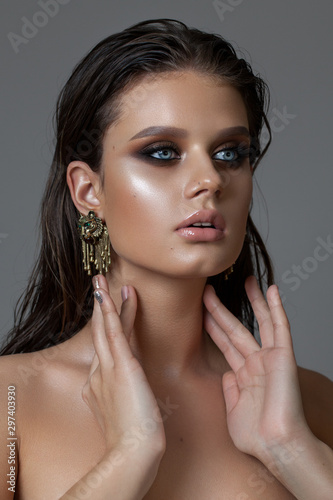 Young beautiful model with a bright blue eyes, fashion make up, perfect skin, fashion earrings and wet hairdo.