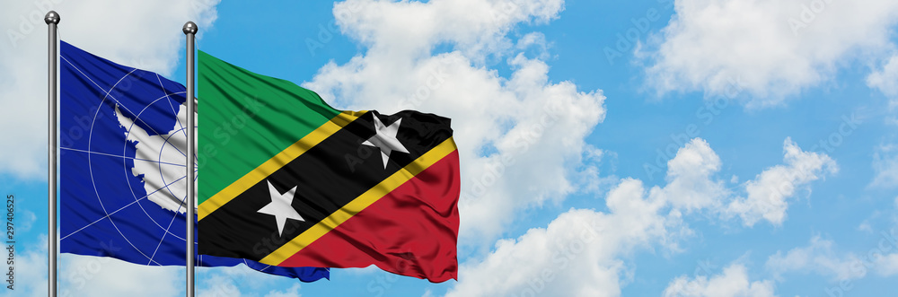 Antarctica and Saint Kitts And Nevis flag waving in the wind against white cloudy blue sky together. Diplomacy concept, international relations.