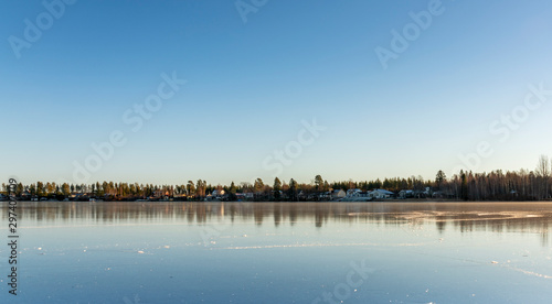 The swedish village lays far away, beside the big crystal clear frozen lake. The surface looks like huge mirror, clear skies, very cold winter day, Northern Sweden © Alexandre Patchine
