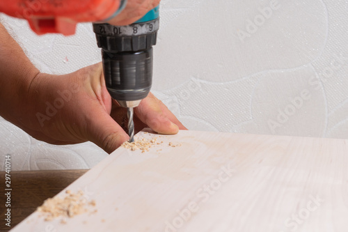 Hands of a craftsman assembling wood chipboard furniture. Drilling holes with a screwdriver.