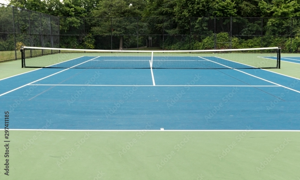 Blue outdoor tennis court with green boarder and trees in background