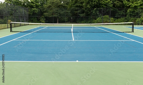 Blue outdoor tennis court with green boarder and trees in background © coachwood