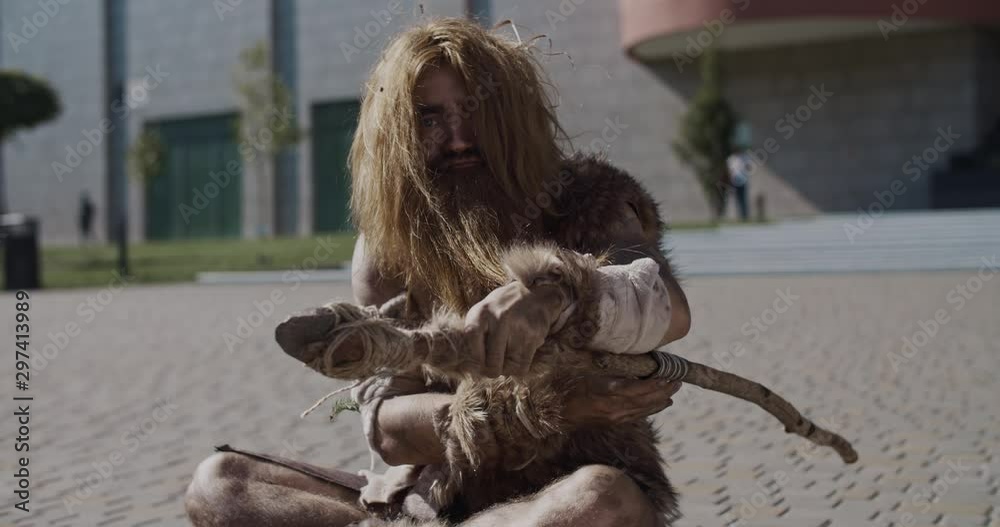 Portrait neanderthal of hunter-gatherers in animal fur holding weapon look at camera serious wants to attack in modern city paleolithic timetraveler evolution civilization slow motion