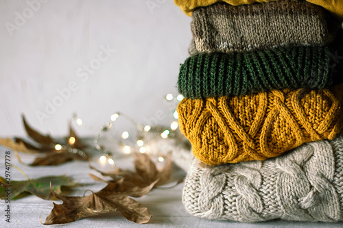 Autumn background. Stack of colorful winter sweaters dray leaves and gloving stars on white wooden background.