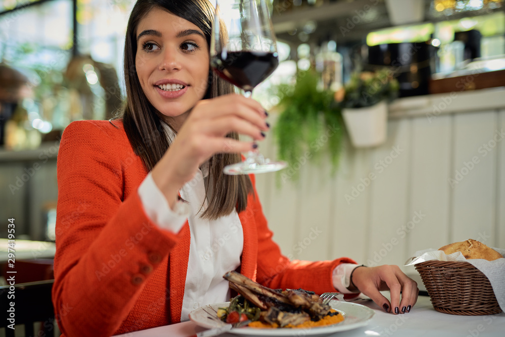 Happy attractive caucasian businesswoman in suit sitting in restaurant for lunch break and drinking red wine.