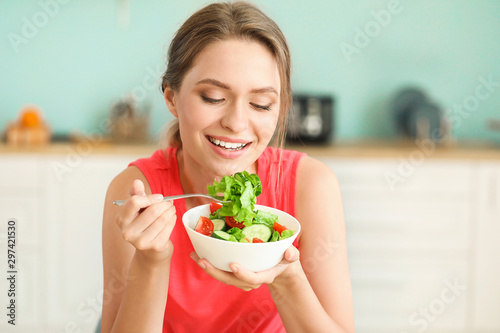 Obraz na plátne Young woman eating healthy vegetable salad in kitchen