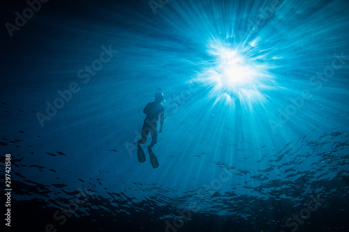 A man snorkeling on water surface, shot from below against the sun. Amazing sun rays peaking through the water surface. Summer adventure, snorkeling, freediving, sport.
