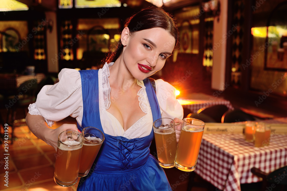 a sexy waiter girl with a big chest in Bavarian clothes holding a lot of beer mugs in the background of the bar during the celebration of the Oktoberfest
