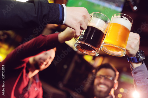 a group of young men s friends in a bar or pub drinking beer with glasses and watching football during the celebration of Oktoberfest