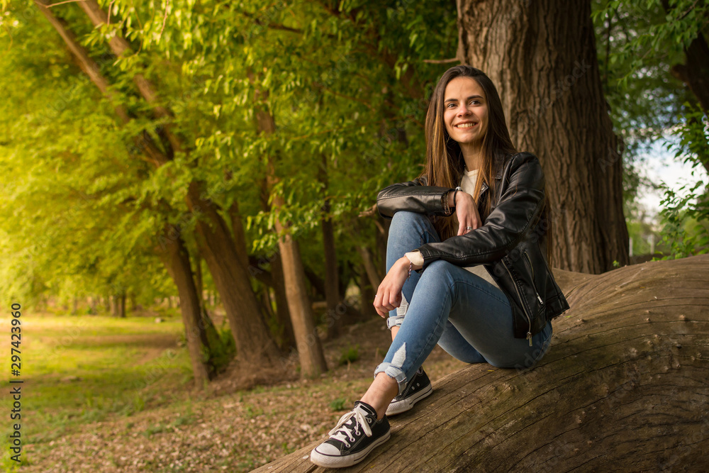 Joven feliz en el bosque sentada sobre tronco en el atardecer