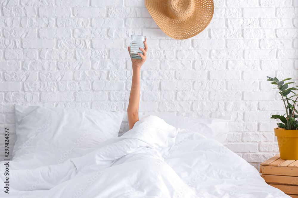 Young woman with glass of water lying in bed - obrazy, fototapety, plakaty 