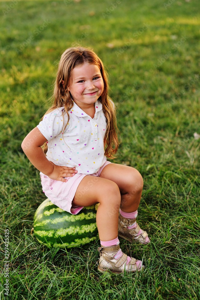 baby little funny girl with red hair leaning on a huge watermelon in the Park on the grass on a summer day baby little funny girl with red hair leaning on a huge watermelon in the Park on the grass on a summer day