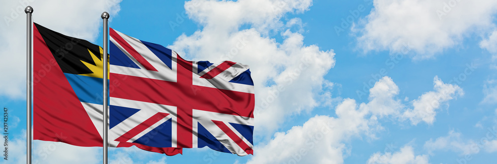 Antigua and Barbuda with United Kingdom flag waving in the wind against white cloudy blue sky together. Diplomacy concept, international relations. Antigua and Barbuda with United Kingdom flag waving in the wind against white cloudy blue sky together. Diplomacy concept, international relations.
